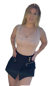 Woman wearing a beige top and black skirt with gold buttons outdoors.